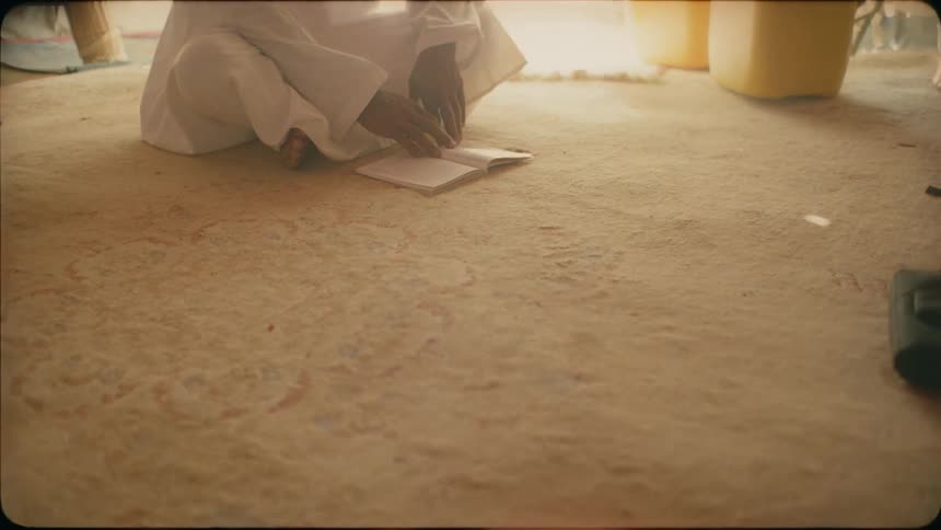 A man sits cross legged on the floor reading a book