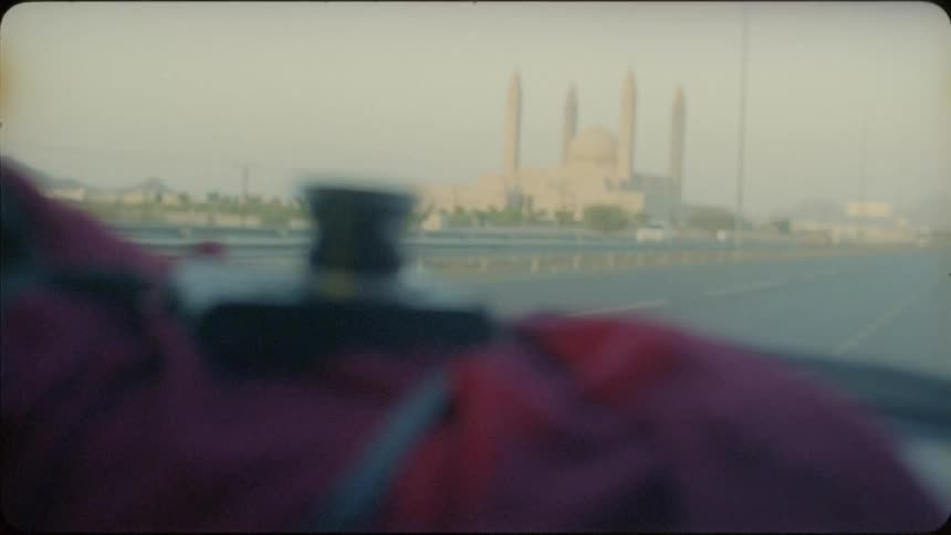 Inside the front seat of a vehicle as it drives past a city with a camera on the dashboard