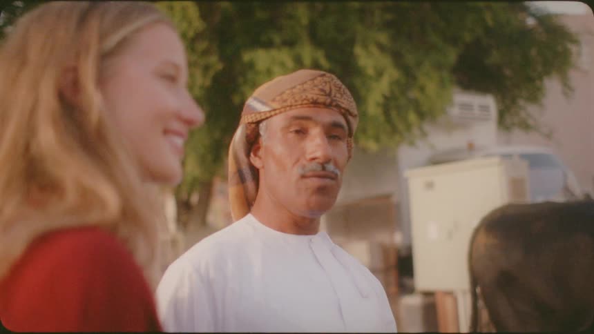 A woman is smiling as an arab man points while they stand outside during the daytime