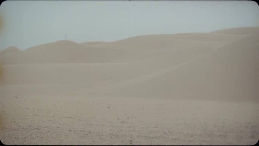 Sand blows in the desert under a blue sky
