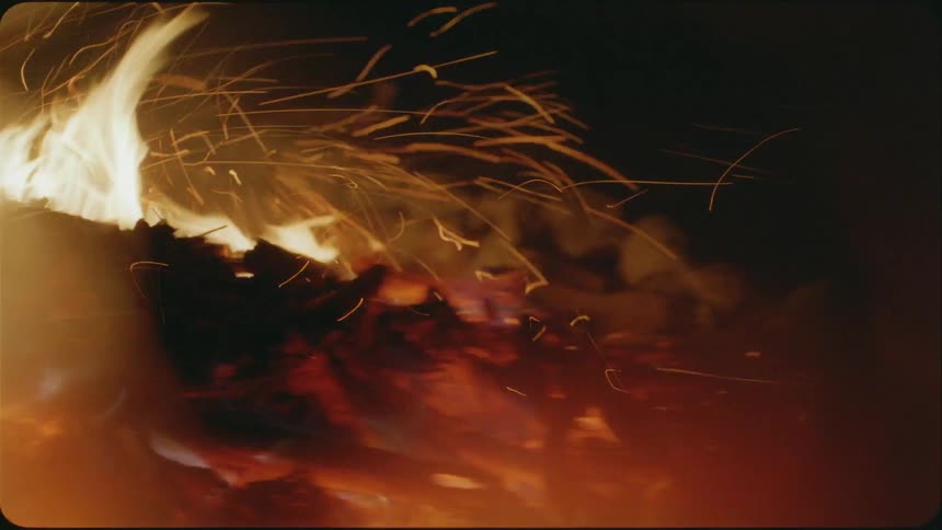 The wind blows sparks and embers from a burning campfire