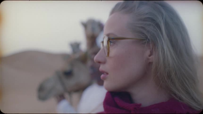 Woman stands near a man who is leading a camel