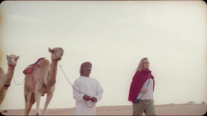 People lead and ride camels through the sand
