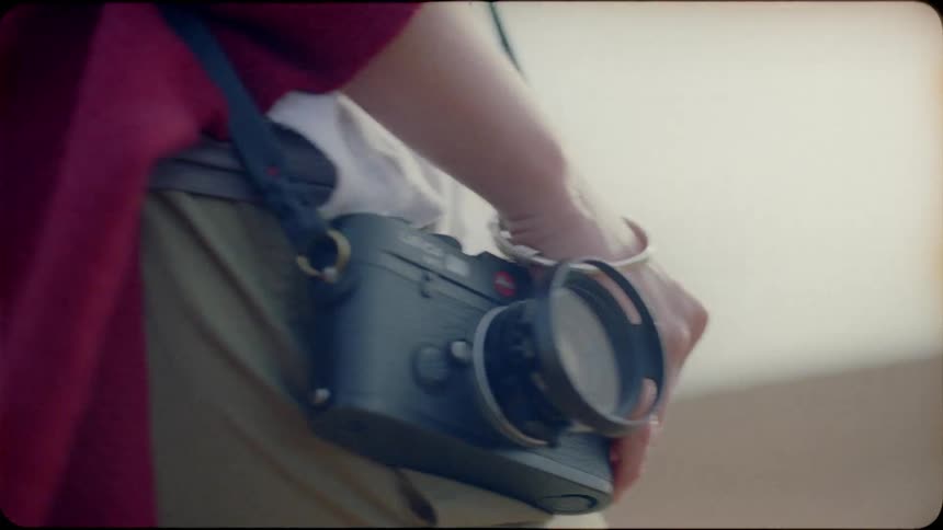 A woman holds onto a camera hanging from a strap on her shoulder