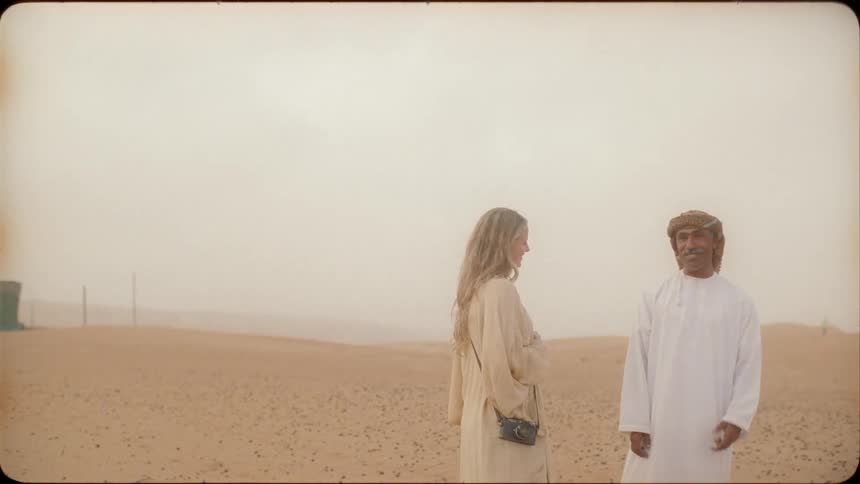 A man and woman talk and laugh while standing in the desert