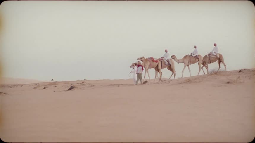 People ride on and lead camels through a desert