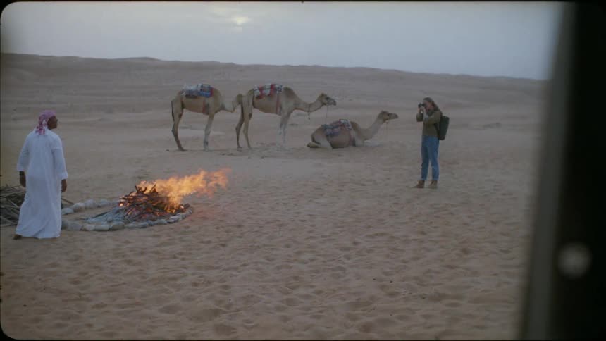 Woman takes a picture of a man standing by a fire in the desert