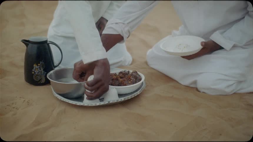 Two middle eastern men eat in the desert