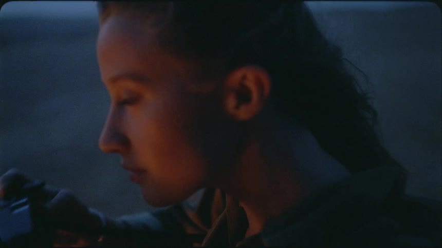 A woman is raising a camera to her eyes as she stands outside at dusk