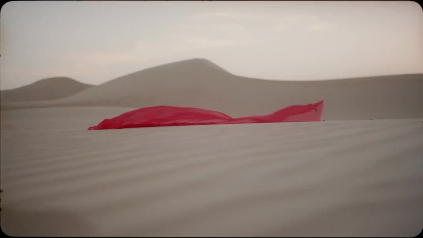 Red veil blows in the wind and lands on the sand in a desert