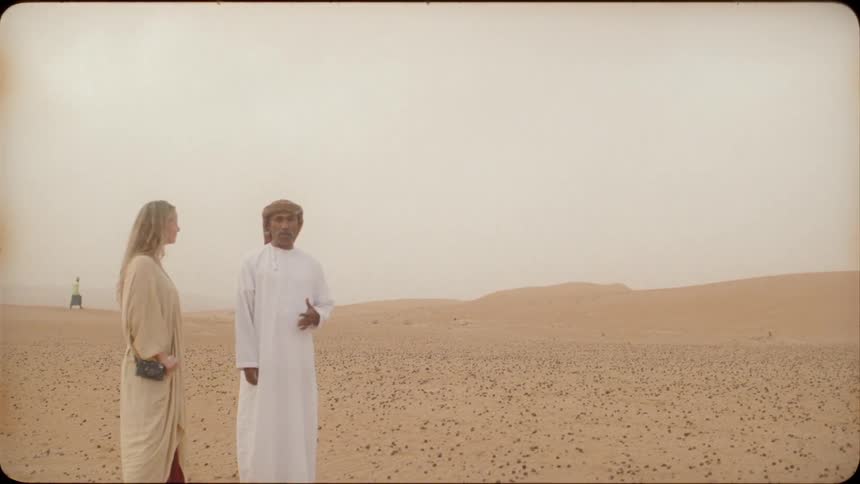 An arab man and a woman are standing in a desert in daylight