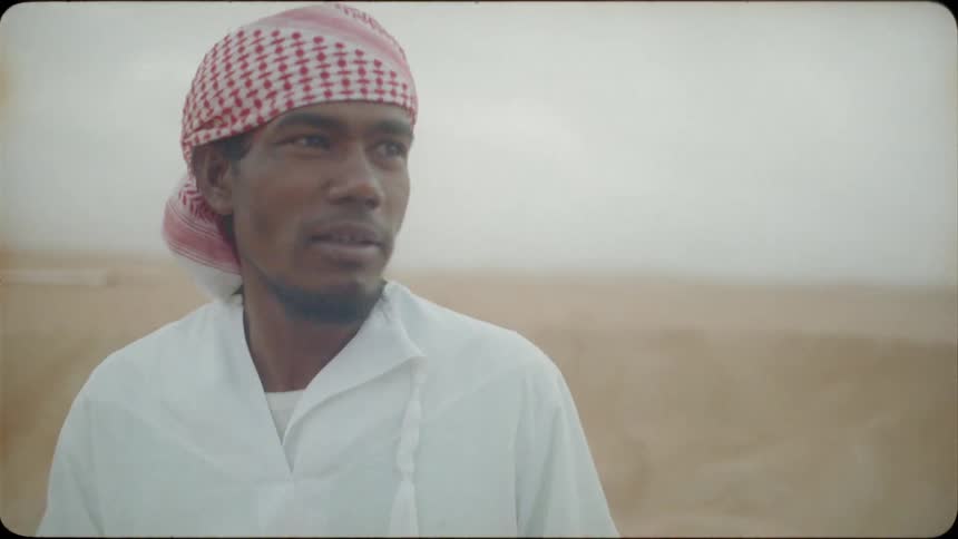 Man wearing a checkered turban talks as he holds a cup