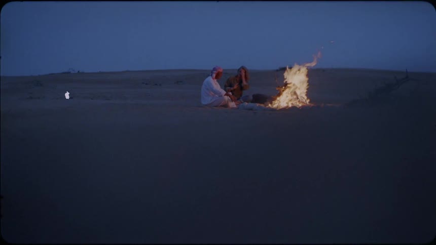 People sit in the desert next to the campfire