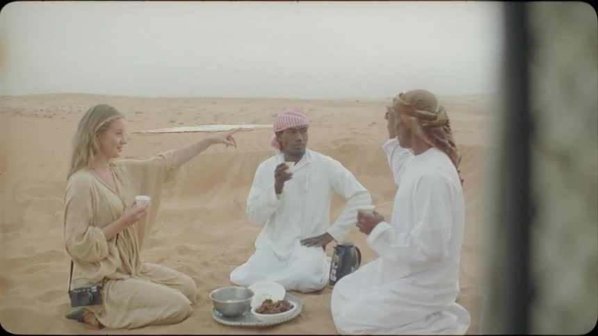 Two men and a woman sit on the sand and talk in the desert