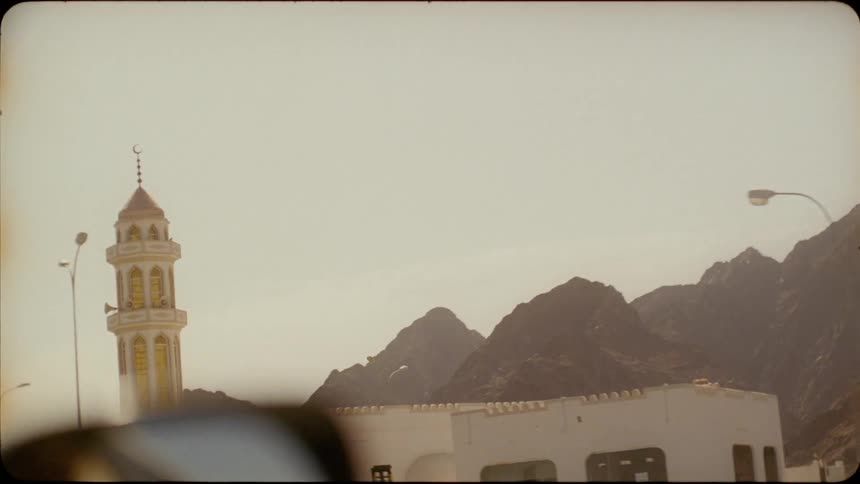 Vehicle travels down a road past buildings near the mountains