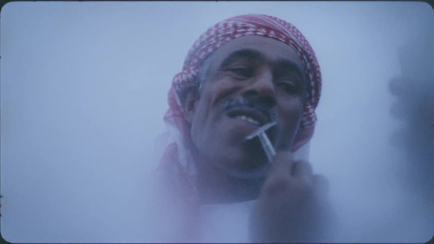 A man shaves his face outside holding a small mirror