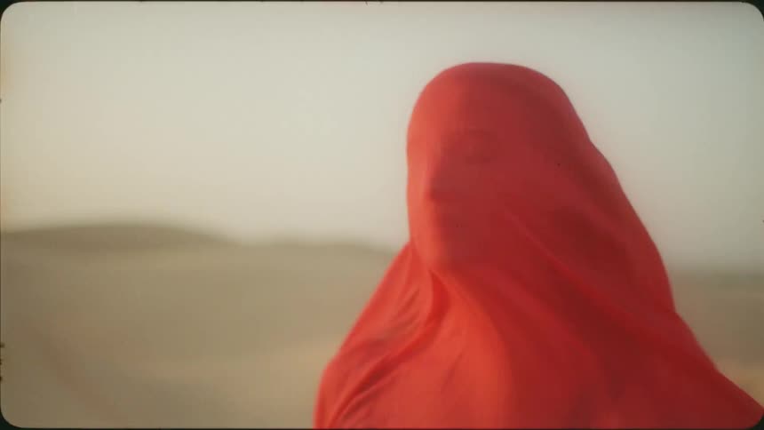Woman standing in a desert covered by a red cloth