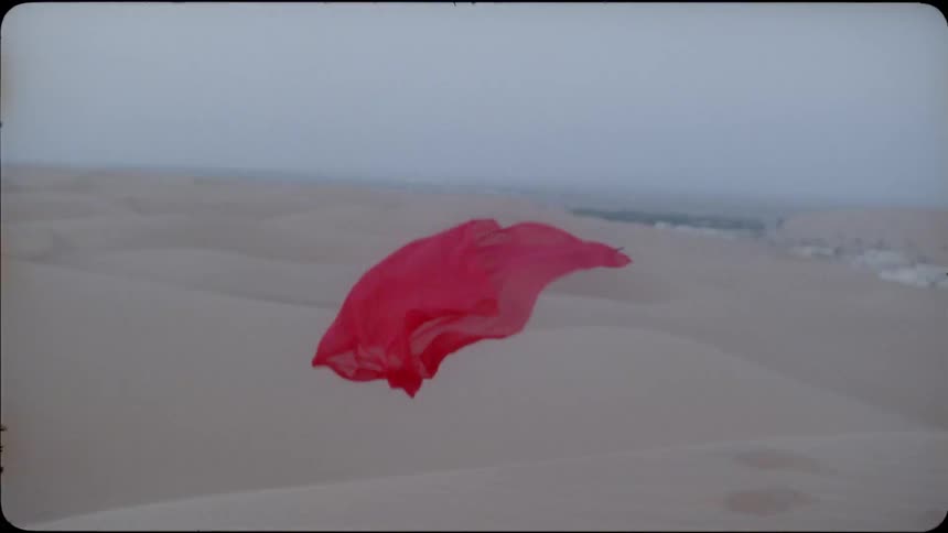 A red scarf veil floats over the desert
