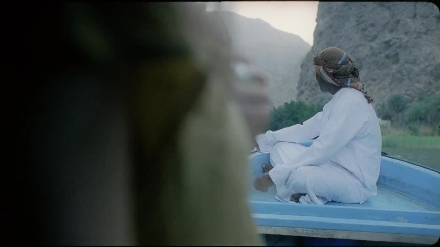 An arab man sitting on a boat smiles then turns his head