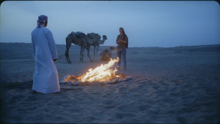 A man and woman stand by a campfire at dawn