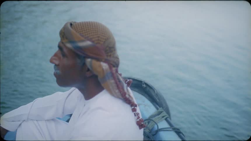 An arab man is sitting in a boat as it floats in a body of water in daylight