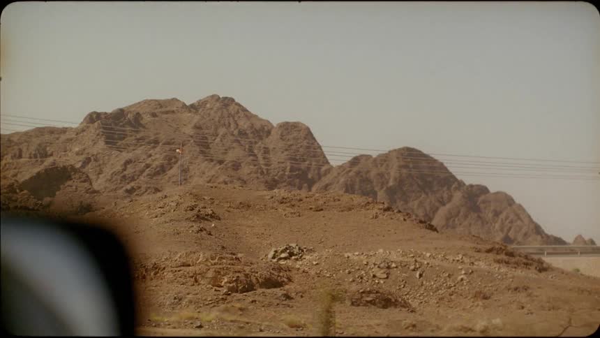 A car drives by rocky mountains in a desert