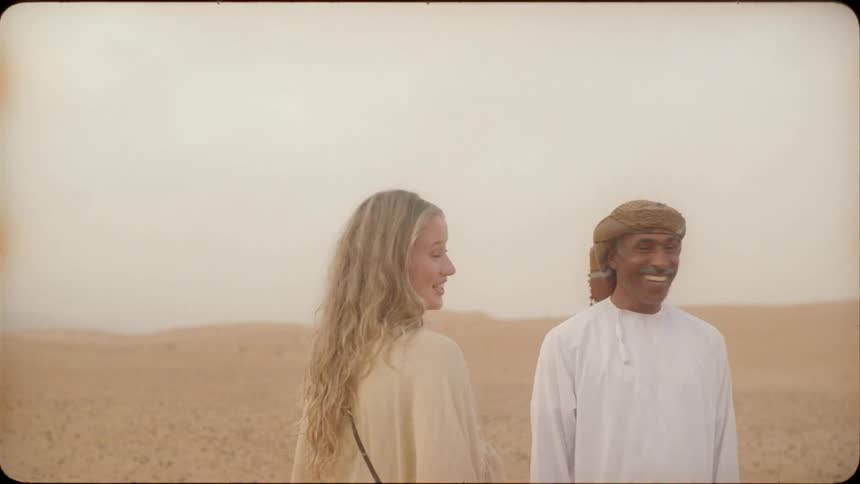 A man and woman talk and laugh while standing in the desert