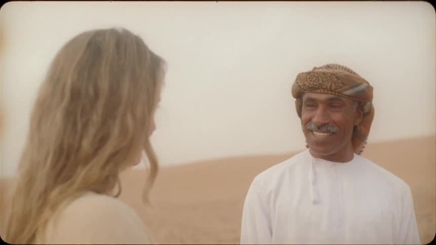 A woman is talking to an arab man as they stand in the desert in daylight