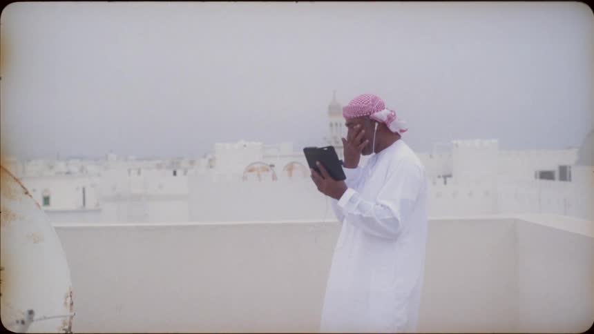 A man laughs as he talks on his phone on a rooftop
