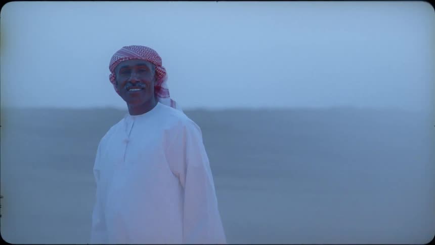 An arab man is standing in the desert on a windy day smiling