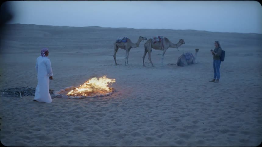 A woman is photographing a man by a campfire