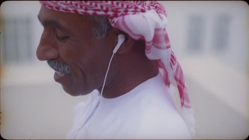 An arab man using headphones smiles and laughs as he talks on a phone