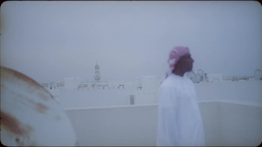 A man standing on a rooftop looks into the distance