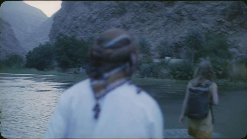 Man follows a woman with a backpack as she walks through the river