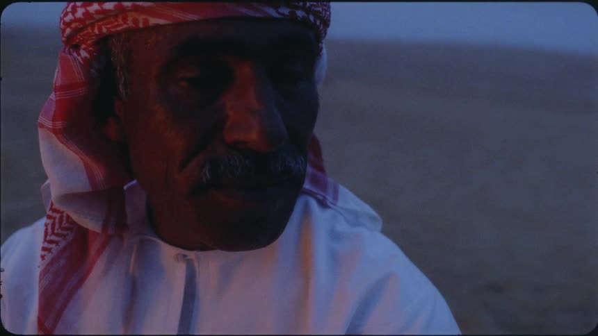 A man looks to his side talking near a campfire