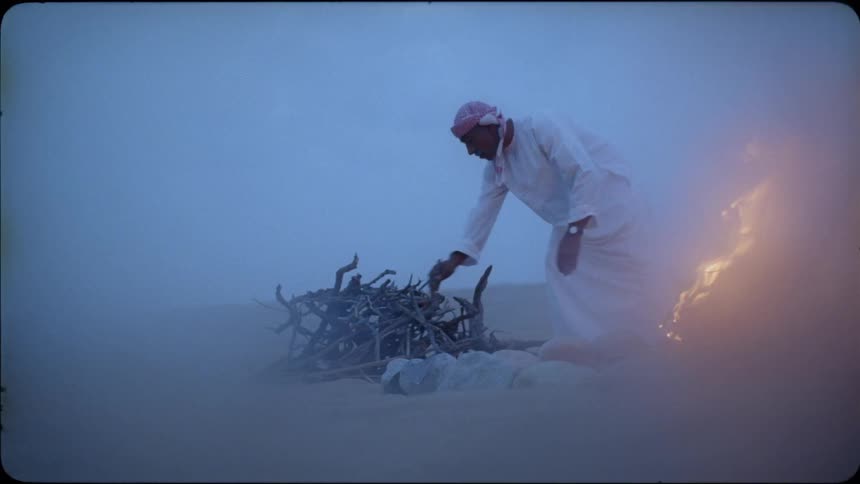 An arab man breaks up branches and adds them to the campfire