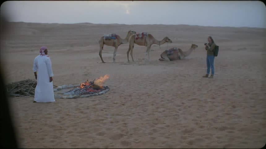 Man stands near a fire while camels are nearby