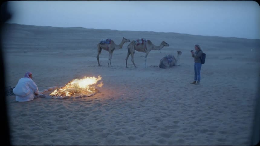 A woman is taking photos of an arab man near a campfire at dusk