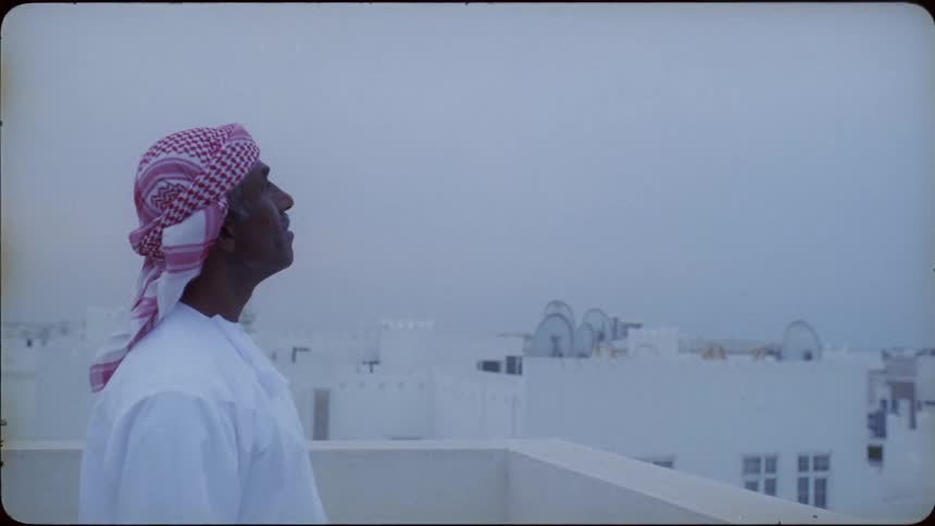 An arab man standing on a rooftop looks up at the sky