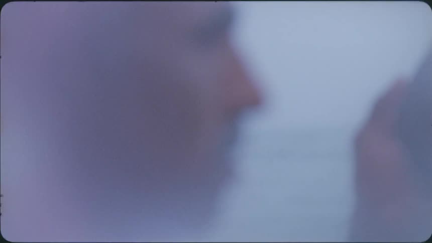 A man looks at his reflection in a piece of mirror while standing outside