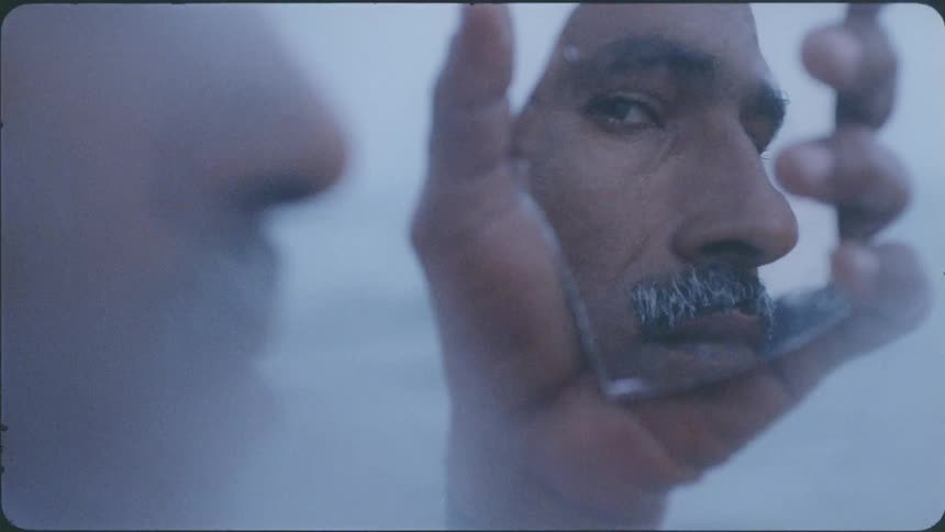 A man's face is reflected in a piece of mirror he is holding