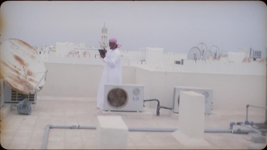 Man stands on a rooftop in a city smiling and looking at a tablet