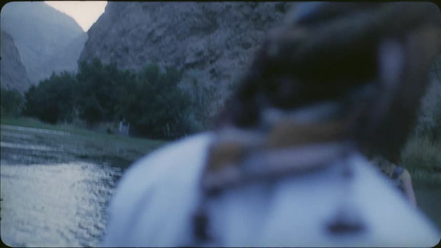 A man follows a woman as they wade across a stream