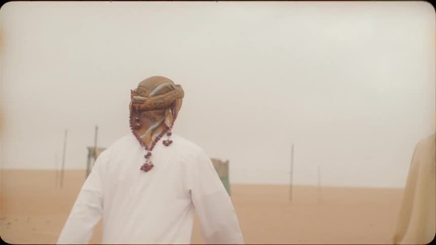 Woman carries a camera as she walks with a man over the sand