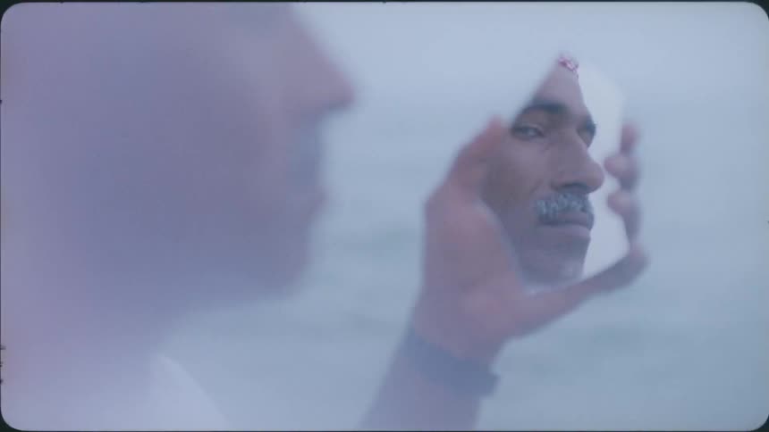 A man holds a mirrored piece of glass to reflect his face