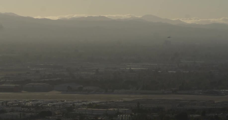 Aerial view of a town below and mountains in the far distance on a foggy day