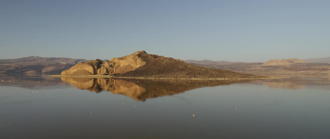 Birds fly over a large flat body of water