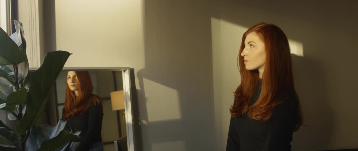 Woman stands near a mirror as she stares straight ahead