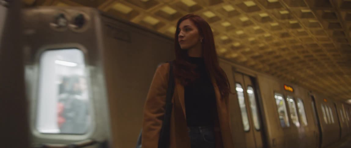 A subway train slows to a stop behind a woman standing on the platform