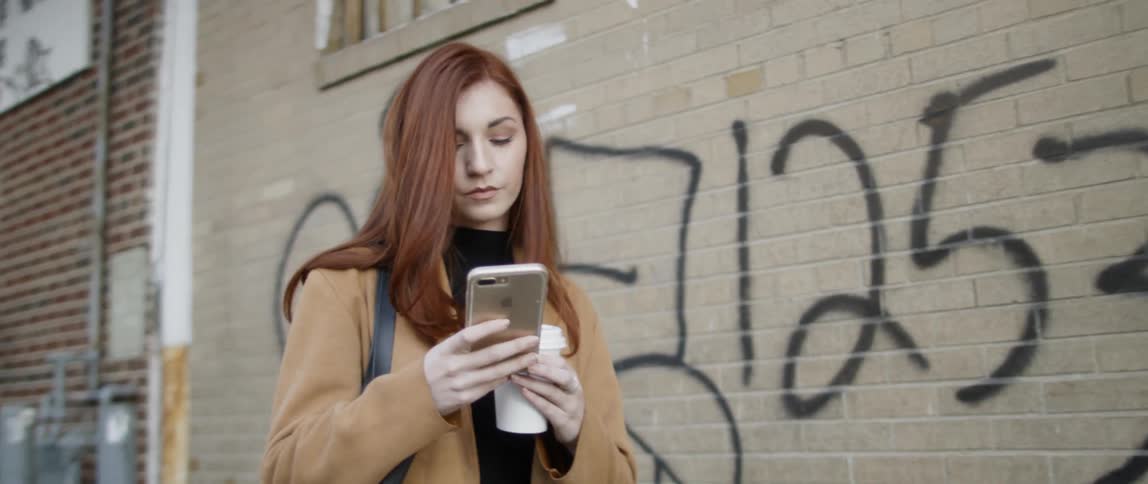 Woman carrying a coffee cup stops and takes her phone out of her pocket